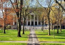 Students walking on a university campus with autumn trees and a historic building in the background