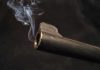 Close-up of a gun barrel emitting smoke against a black background