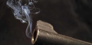 Close-up of a gun barrel emitting smoke against a black background