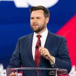 Man speaking at a podium, wearing suit and tie.