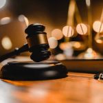 Gavel on wooden table with scales in background.