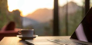Laptop, coffee cup, and phone on wooden table.