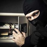 A masked burglar holding a gun while attempting to open a safe