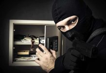 A masked burglar holding a gun while attempting to open a safe