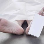 Feet of a deceased person covered by a white sheet with an identification tag