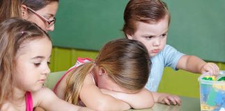 Children at a table with building blocks, one child appears upset