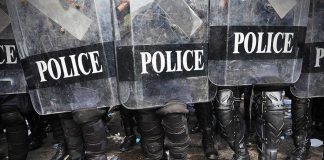 Police officers in riot gear standing behind shields marked POLICE
