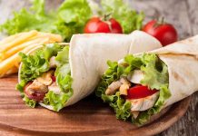 Two chicken wraps filled with lettuce and tomatoes on a wooden plate with fries