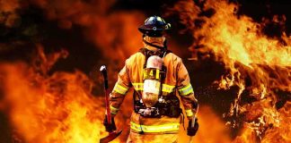 Firefighter standing in front of a large fire, equipped with tools