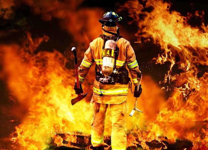 shutterstock_80081197.jpg Firefighter standing in front of a large fire, equipped with tools