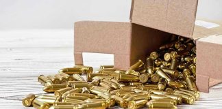 Box of brass bullets spilled on wooden surface.