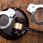 Gavel and handcuffs on wooden surface.