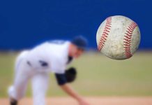 A baseball in mid-air with a pitcher in the background preparing to throw