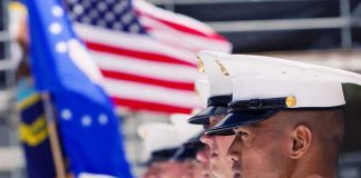 Marines in uniform standing in formation with flags in the background