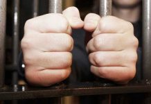 Hands gripping jail cell bars tightly.