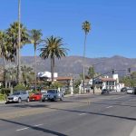 Street with cars, palm trees, and mountains in the background.