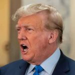 Trump TORCHES First American Pope Man in suit with open mouth, speaking passionately.