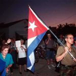 Cuban Dictator’s SHOCKING Indictment Imminent! A group of people participating in a protest march holding a Cuban flag