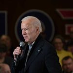 Biden’s BIZARRE Exit Sparks New Mystery Man speaking into a microphone at an event.