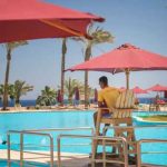 Lifeguard overlooking a resort swimming pool with red umbrellas