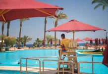 Lifeguard overlooking a resort swimming pool with red umbrellas