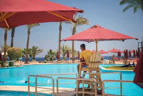 Lifeguard overlooking a resort swimming pool with red umbrellas