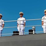 three naval officers in white uniforms standing on a ship deck