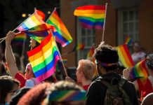 Crowd waving rainbow flags at an outdoor event