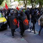 masked protesters march with shields on a city street