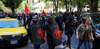 masked protesters march with shields on a city street
