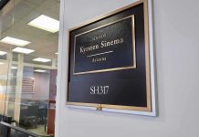 Office door plaque with gold trim outside a glass-walled conference room