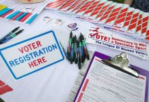 Voter registration table with forms, pens, and informational materials