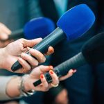 Largest Denaturalization Crackdown Recorded History Underway Reporters holding colorful microphones