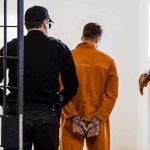 Prisoner in orange jumpsuit handcuffed and escorted by officer