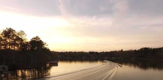 Boat wake curving across a calm lake at sunset