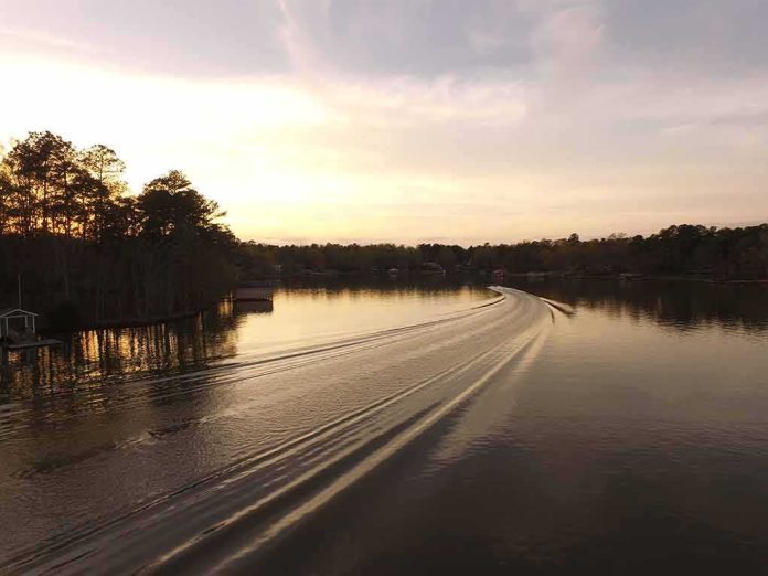 Boat wake curving across a calm lake at sunset