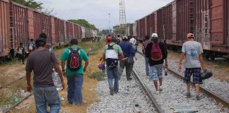 Group of people walking along railroad tracks between freight trains