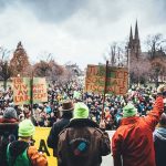 DSA to Illegals: ‘You Don’t Need Papers’ Christian Jones at a large outdoor protest with crowds and handmade signs