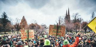 Christian Jones at a large outdoor protest with crowds and handmade signs