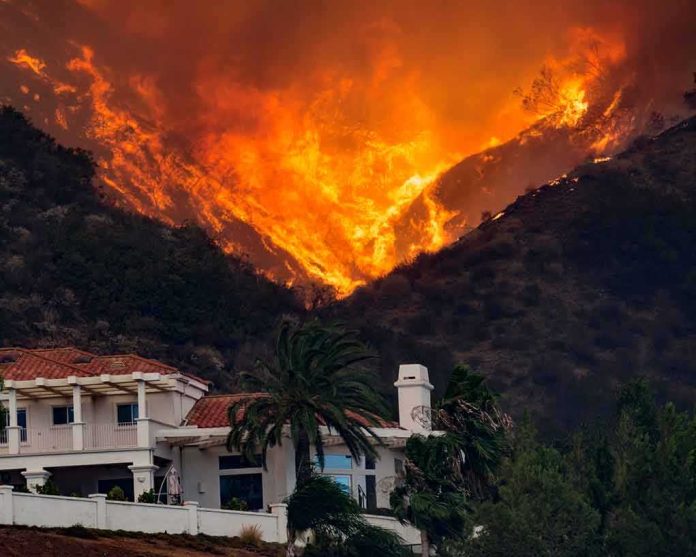 Wildfire engulfs hillside behind a suburban house
