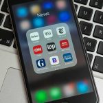 High School Coach ARRESTED – Player Makes Shocking Find Smartphone displaying a folder of news apps on a laptop keyboard