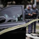 Car door with bullet holes at a taped-off crime scene