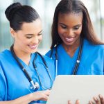 Two nurses in blue scrubs looking at a tablet
