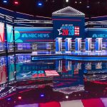 Televised debate stage with multiple podiums and bright red, white, and blue lighting