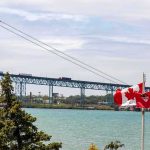 Suspension bridge over a river with Canadian flags in the foreground