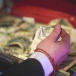 Hand holding cash over an open briefcase filled with money