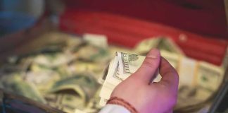 Hand holding cash over an open briefcase filled with money