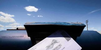 Mail-in ballot being inserted into a blue USPS mailbox