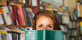 Woman holding a green book in front of her face in a library