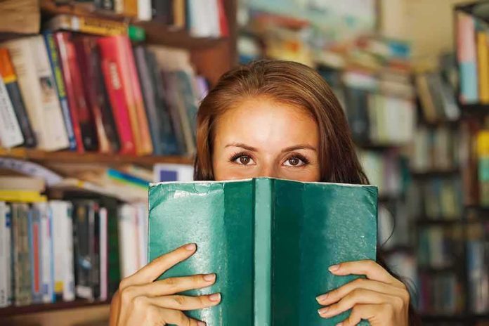 Woman holding a green book in front of her face in a library